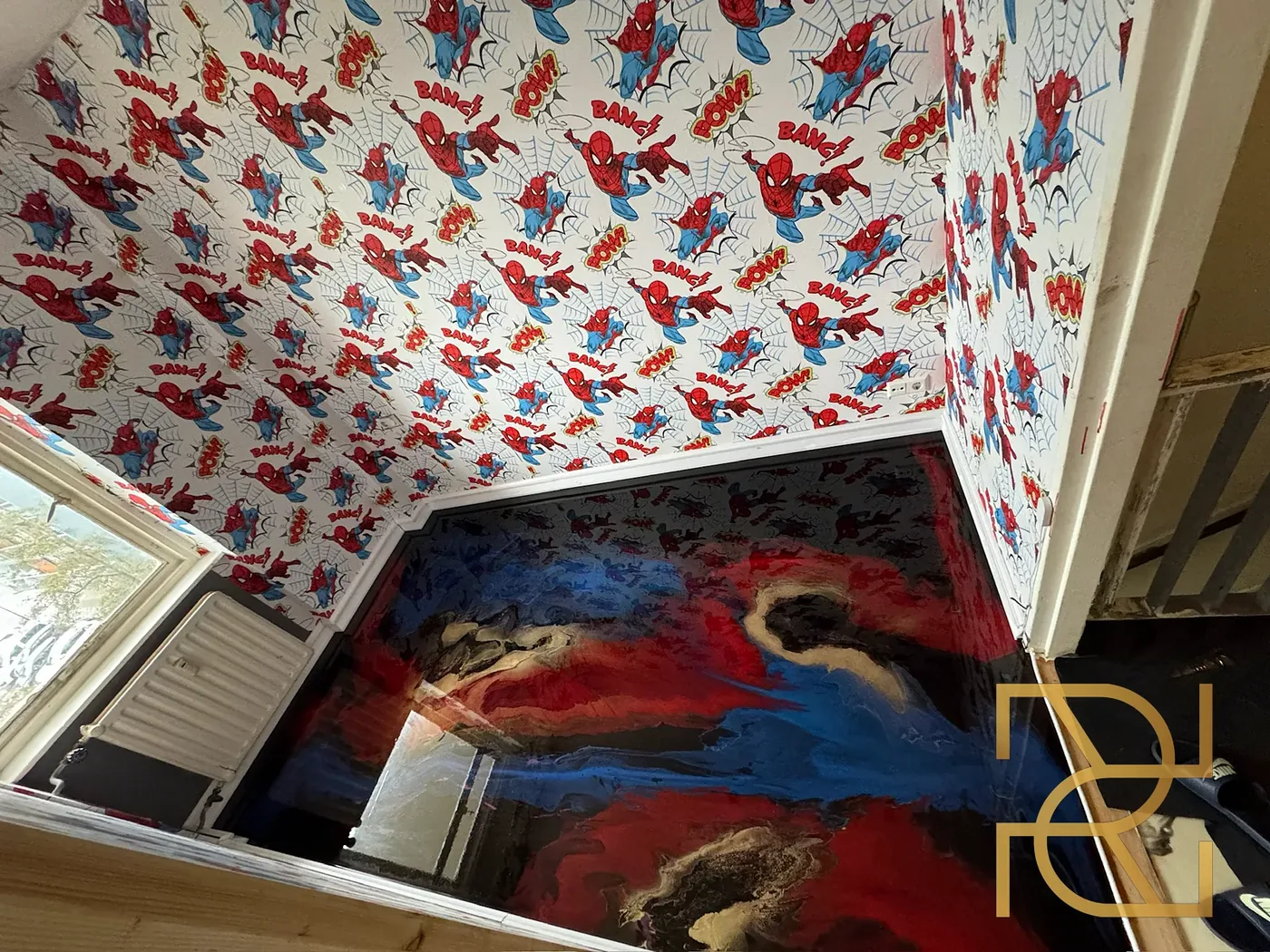 De Spider-Man-kamer bij daglicht: de gietvloer met rood, kobaltblauw, zwart en goudaders spiegelt het behang